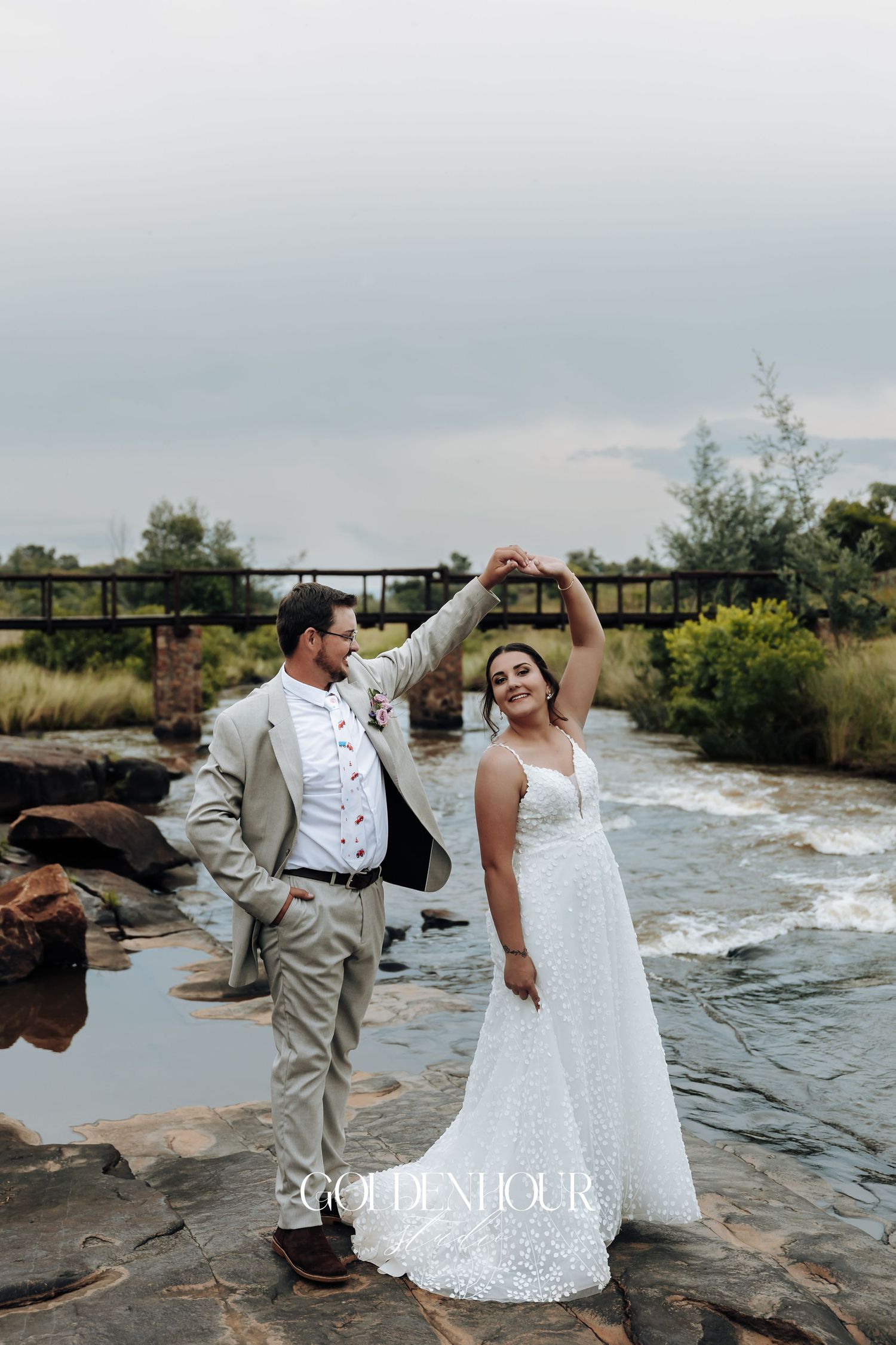 Couple dances and poses on stone surface near water during wedding photoshoot.
