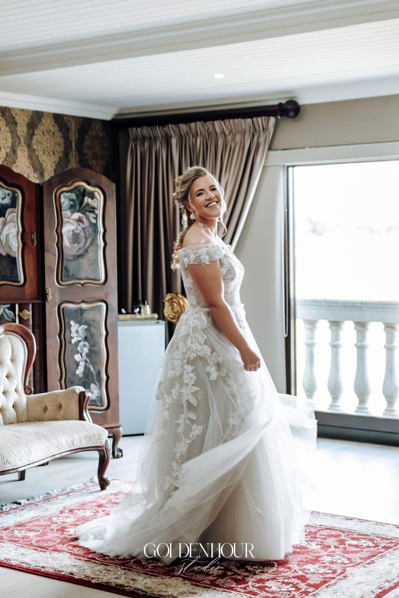 Joyful bride twirling in lace off-shoulder wedding dress in elegantly decorated room.