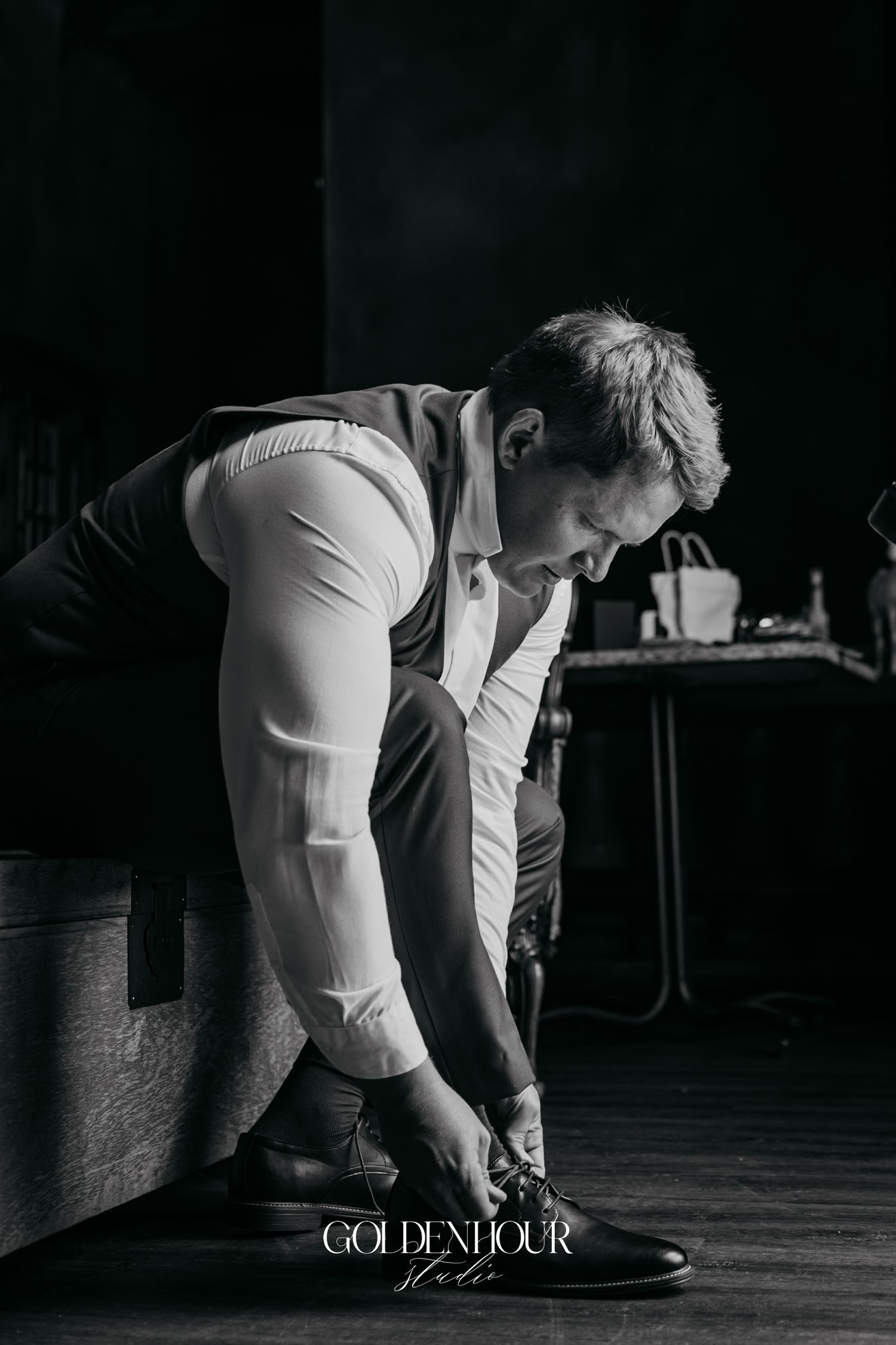 Black and white photo of a groom tying his dress shoes while getting ready for his wedding day.