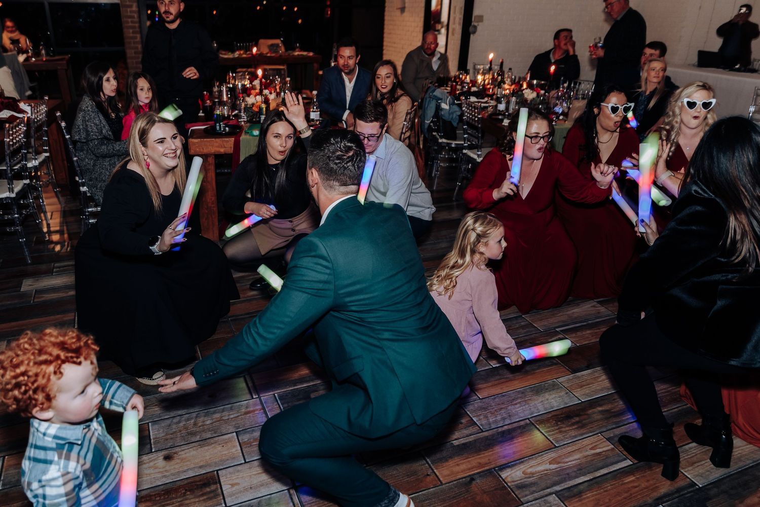 Guests dancing with colorful glow sticks at a lively indoor wedding reception party.