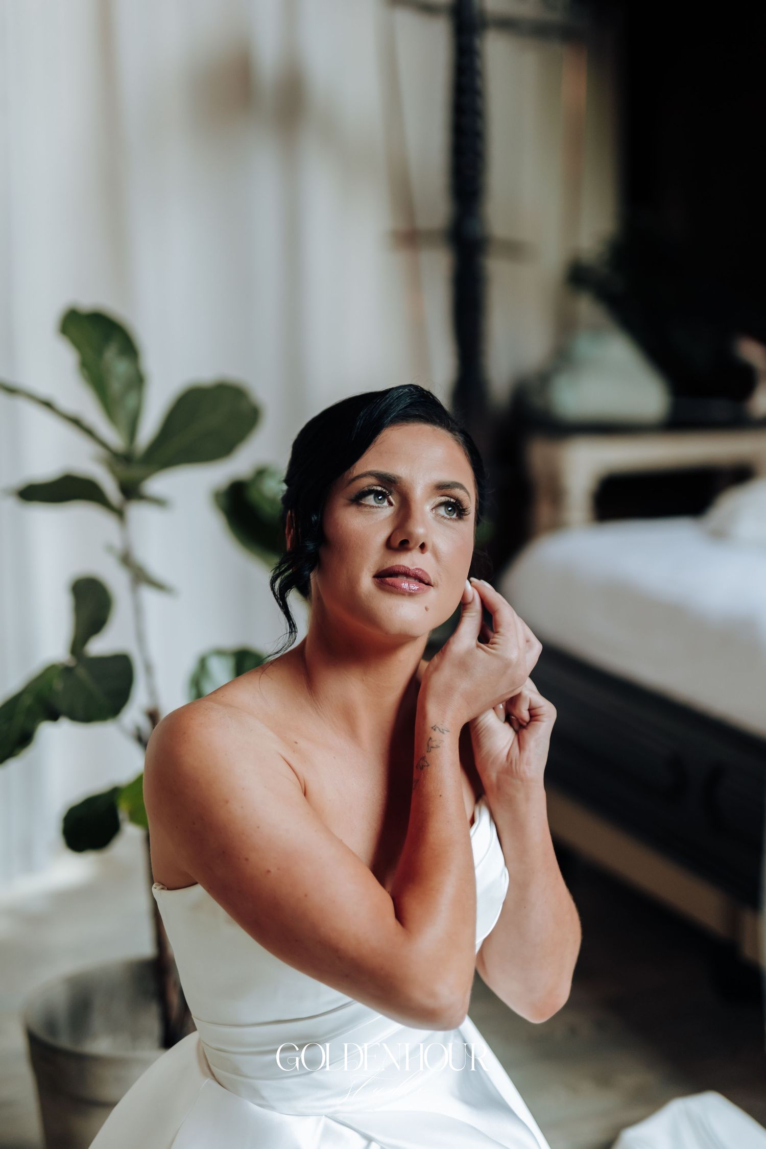 Beautiful bride in a strapless white gown putting on earrings while getting ready in a modern styled room.