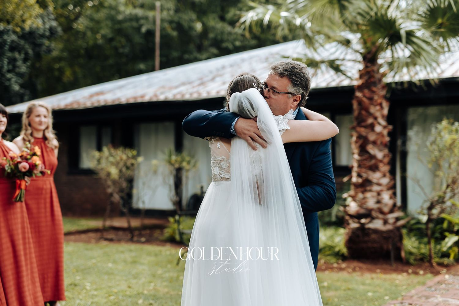 Emotional bride and older gentleman share a warm embrace outdoors during wedding day first look moment.