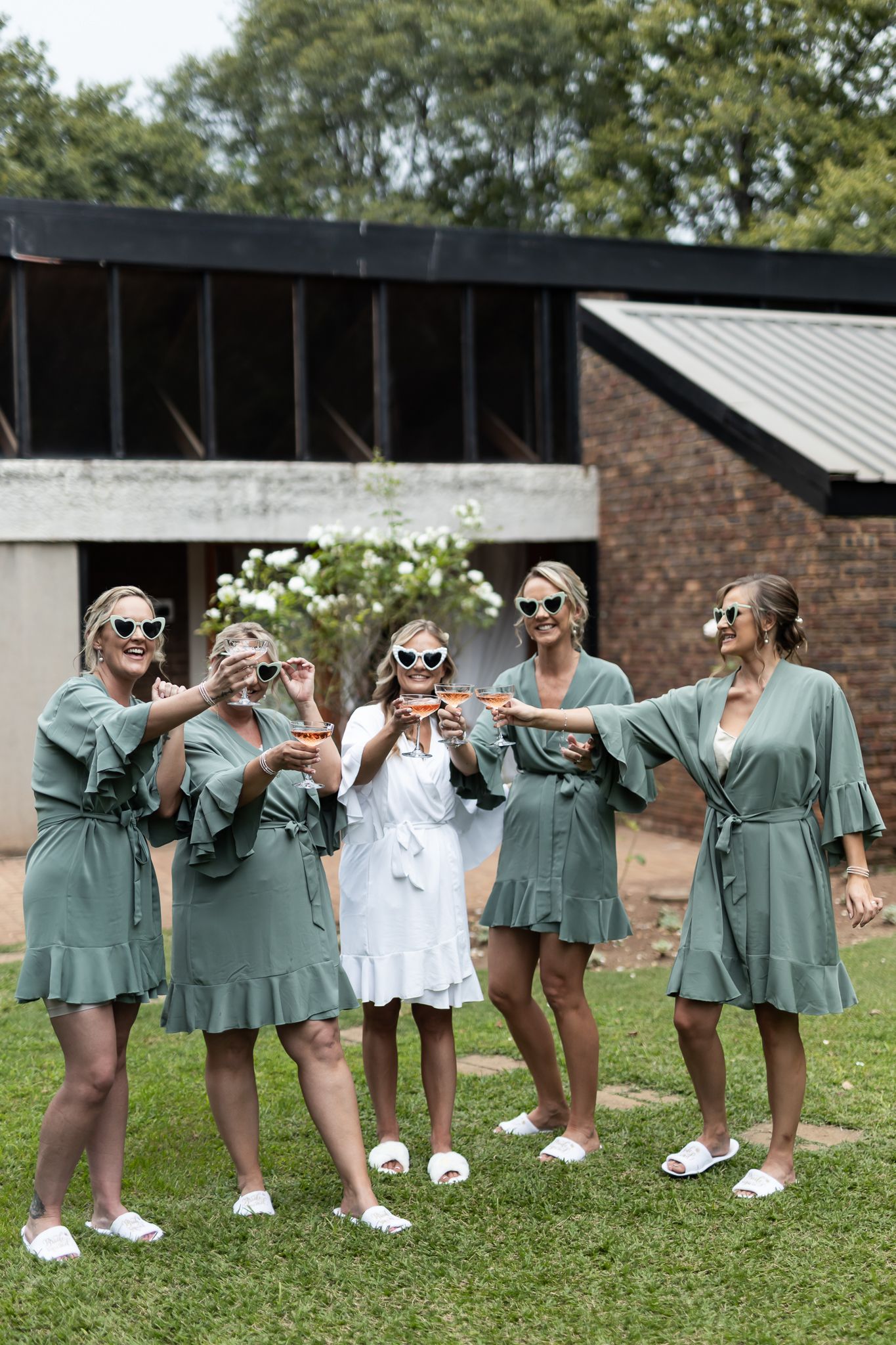 Bridal party in sage robes and sunglasses having fun posing together outdoors.