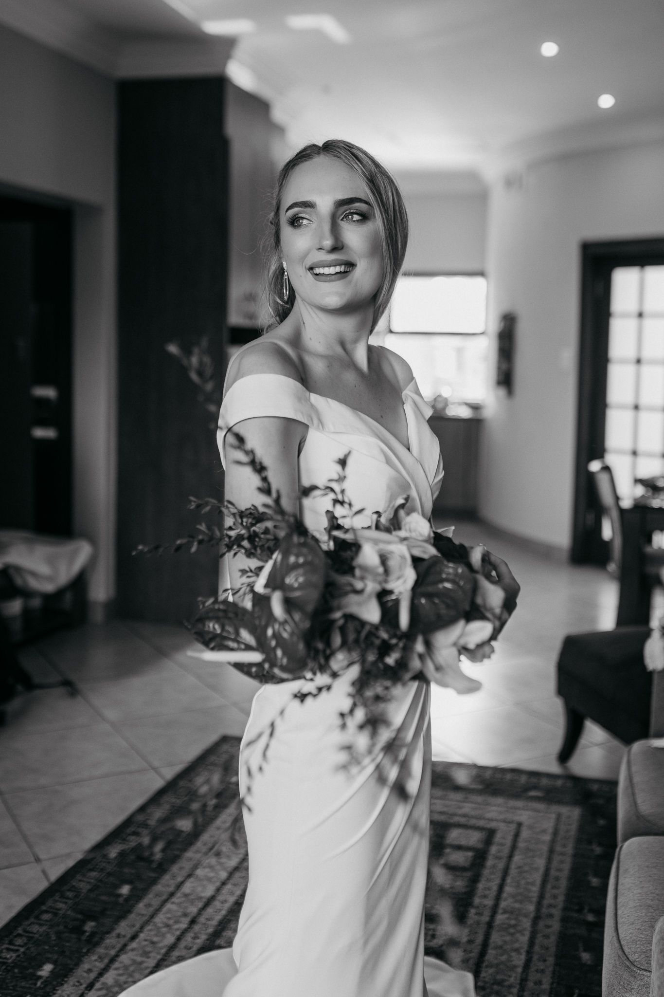 Black and white portrait showcasing elegant off-shoulder wedding dress and bouquet.