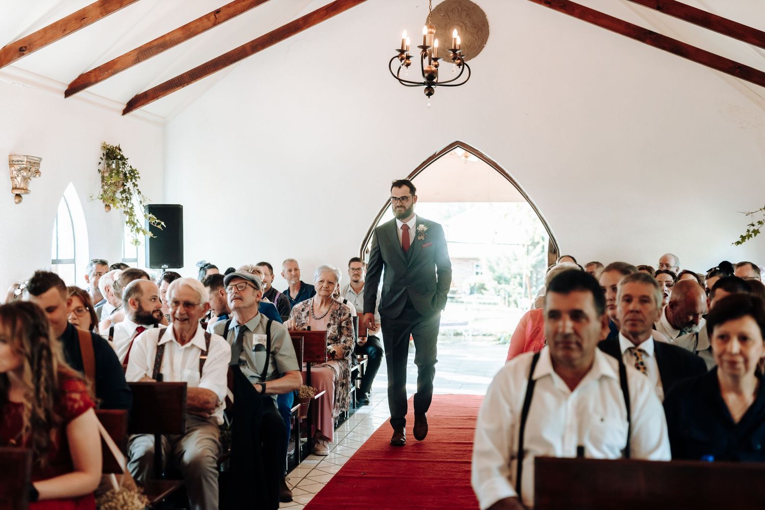 A joyful wedding ceremony inside a chapel with wooden beams and a red carpet aisle.