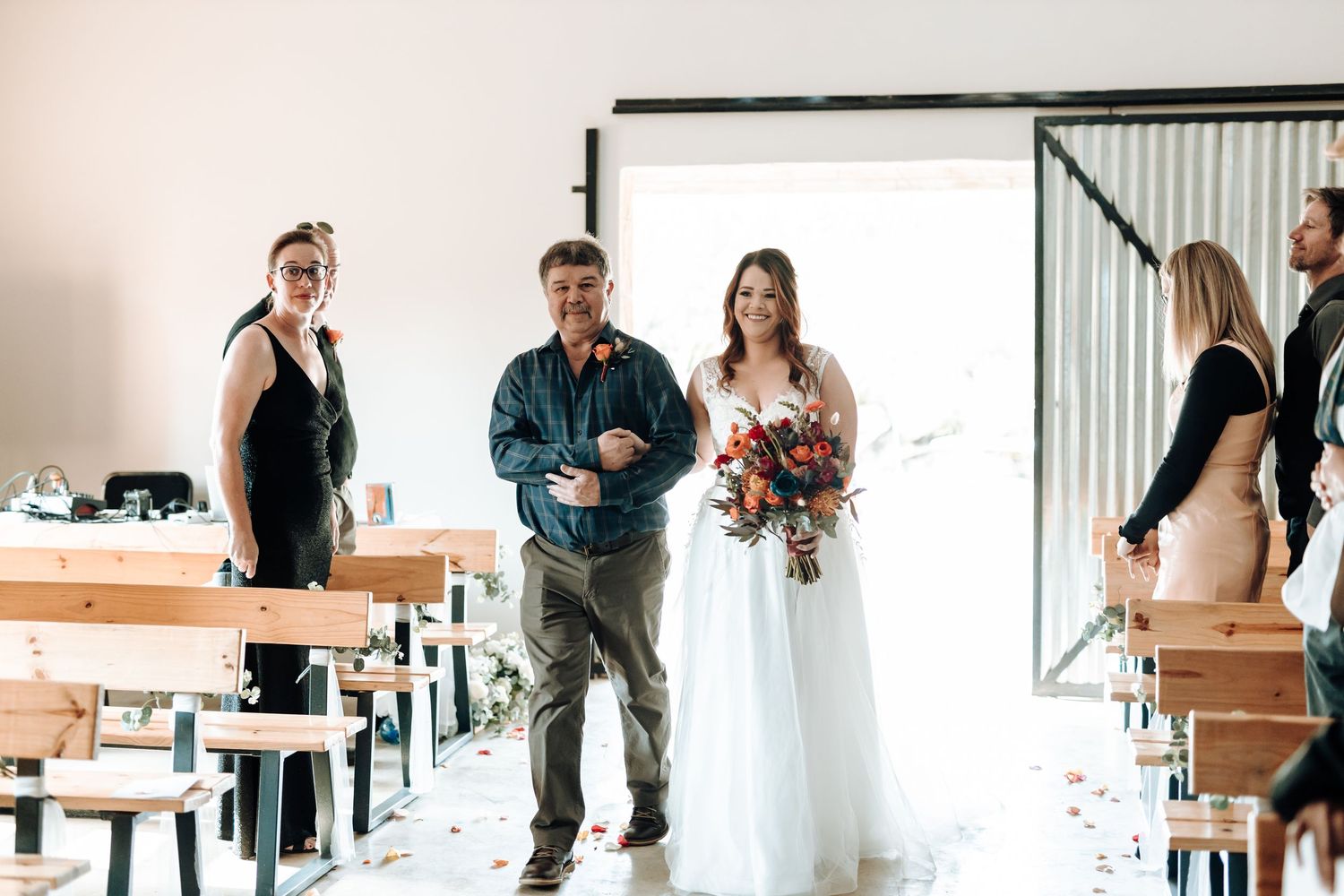 Wedding ceremony processional in modern rustic venue with wooden bench seating.