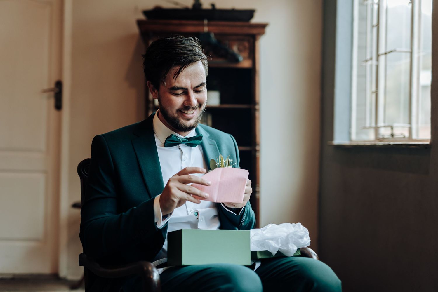 Wedding preparation moment shows suited person reading card beside wrapped gift.