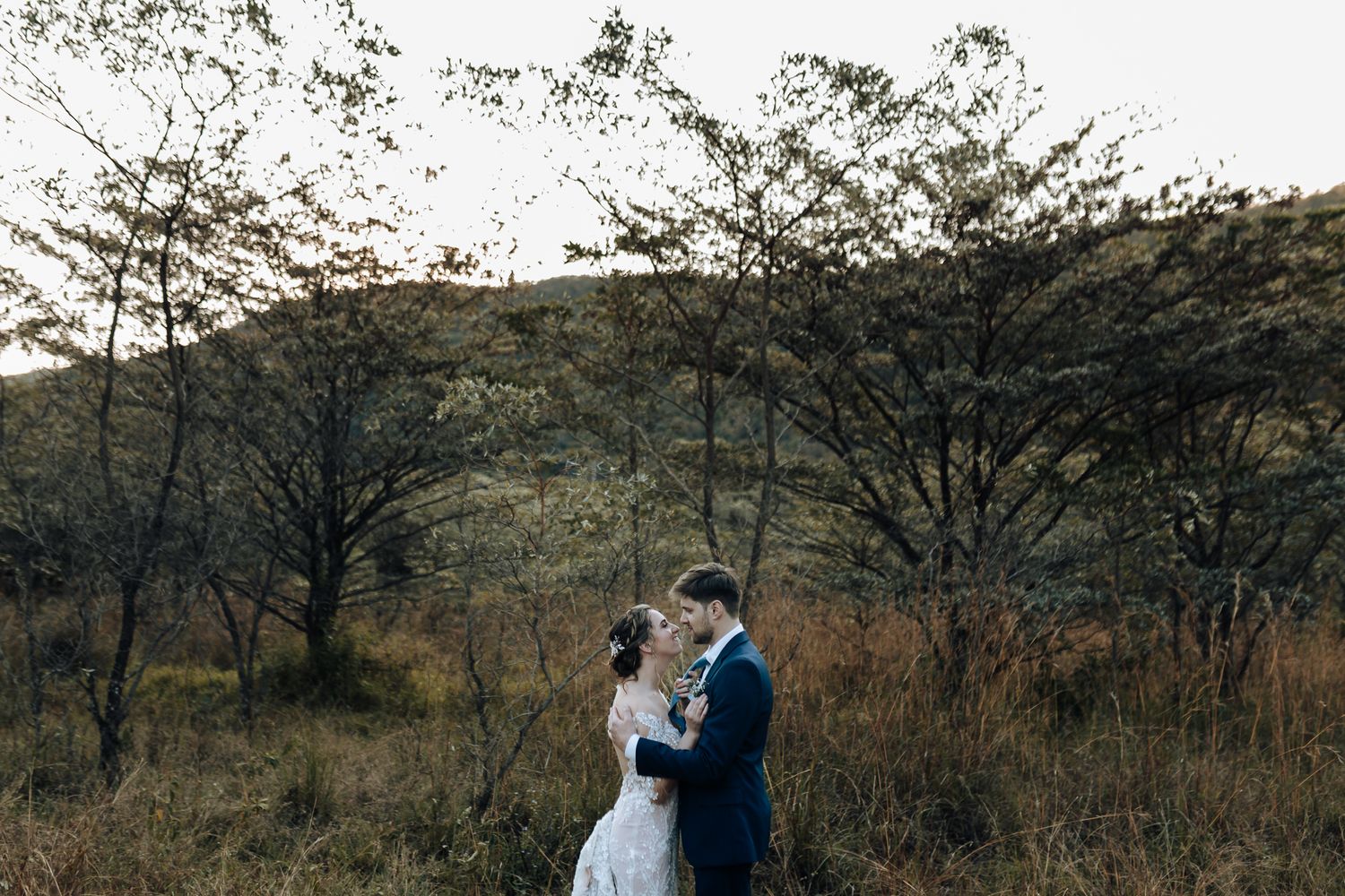Artistic wedding photo capturing couple's silhouette against mountainous landscape at sunset.