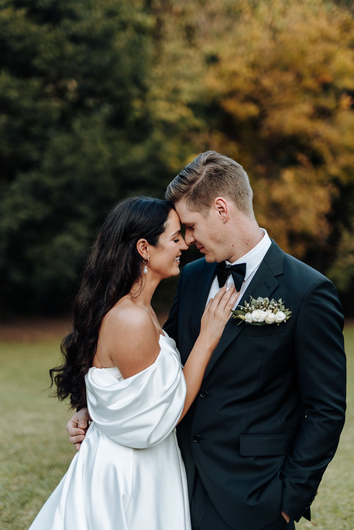 Romantic wedding portrait with couple sharing intimate moment against autumn backdrop.