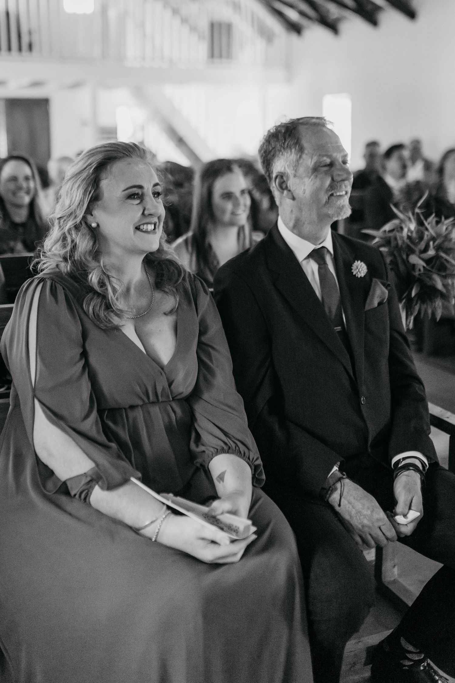 Black and white photo of wedding guests laughing together during an emotional moment at a ceremony.