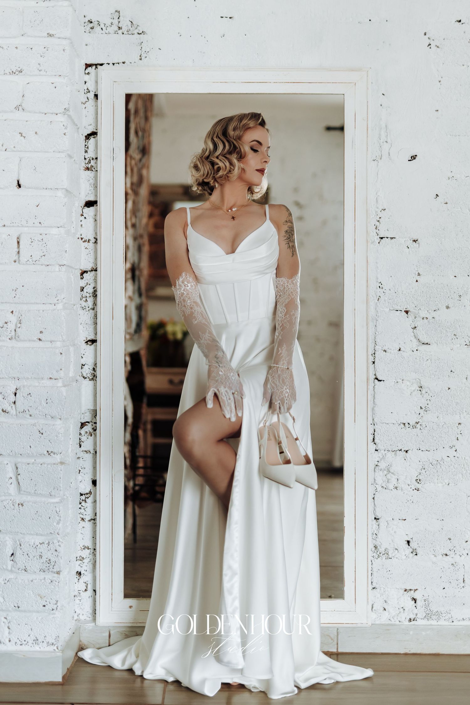 Flowing white wedding dress displayed in bright minimalist setting with white brick walls.