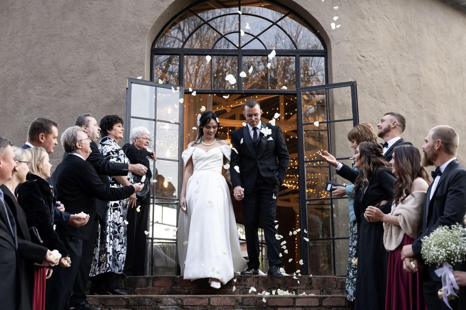 Wedding guests gather in celebration inside an illuminated stone building with string lights overhead during a reception.