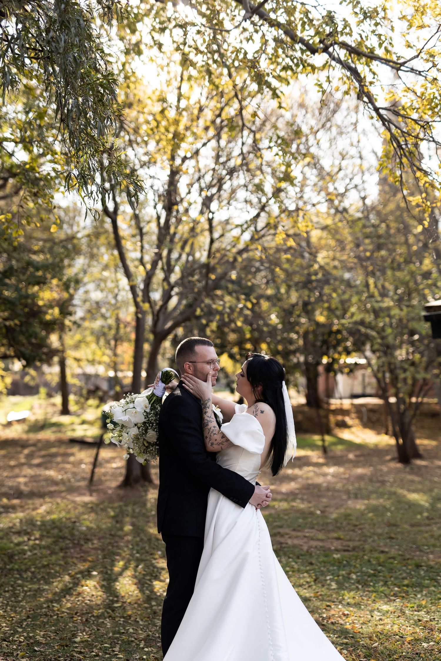 A couple shares an intimate moment among autumn trees in a park setting on their wedding day.