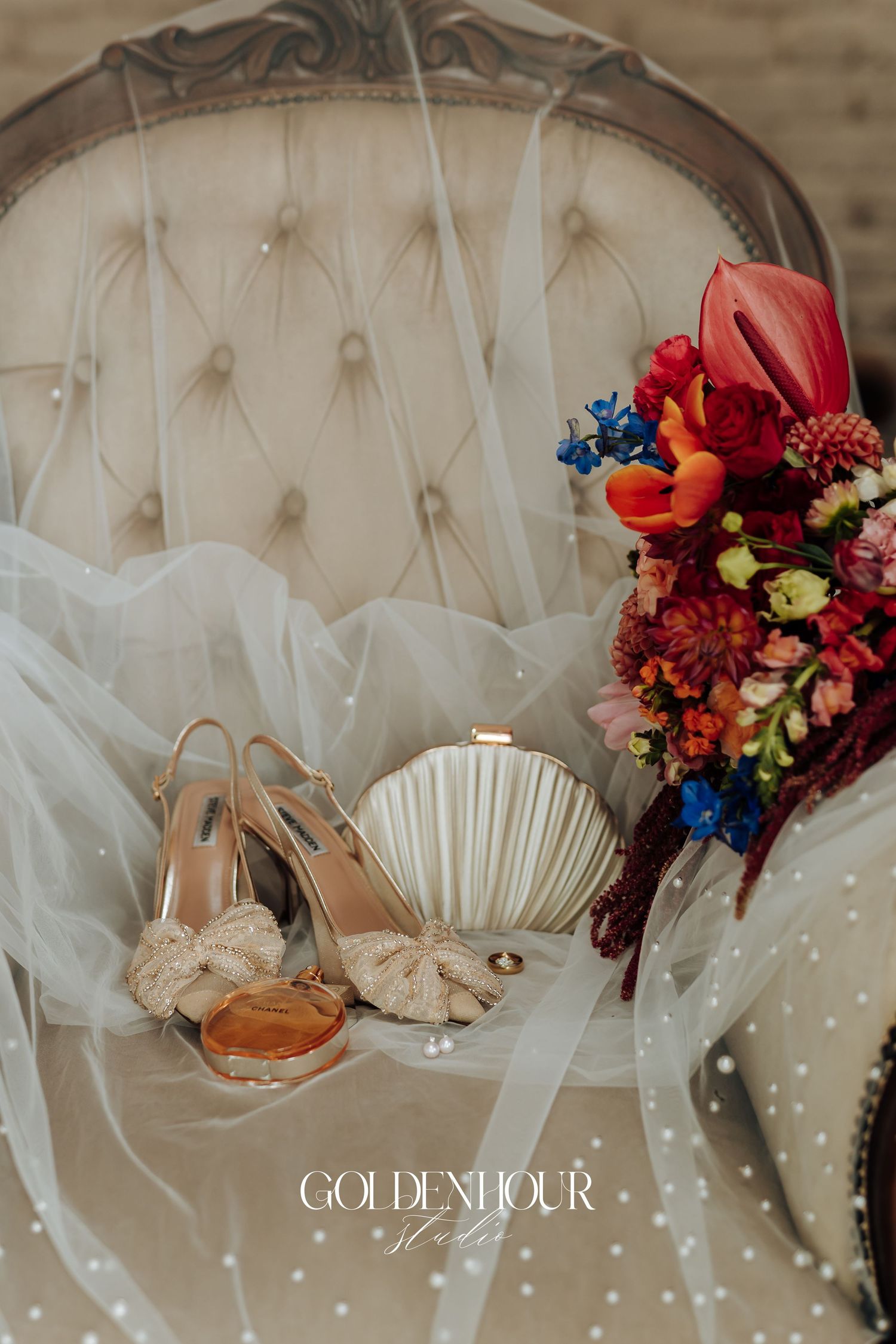 Elegant tufted beige couch with delicate tulle fabric and vibrant red and orange floral arrangements.