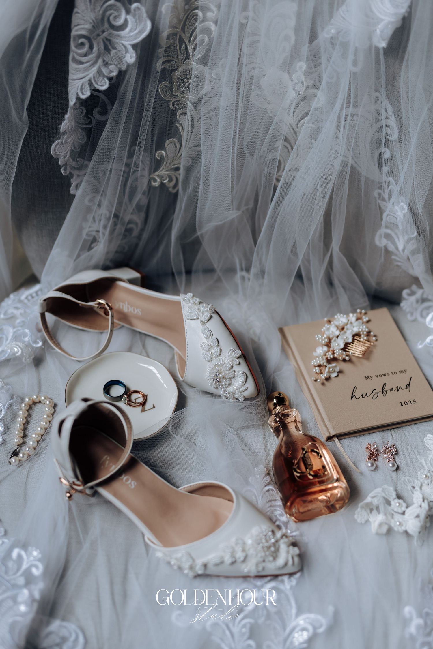 Wedding accessories including shoes, rings, and veil arranged on white lace.