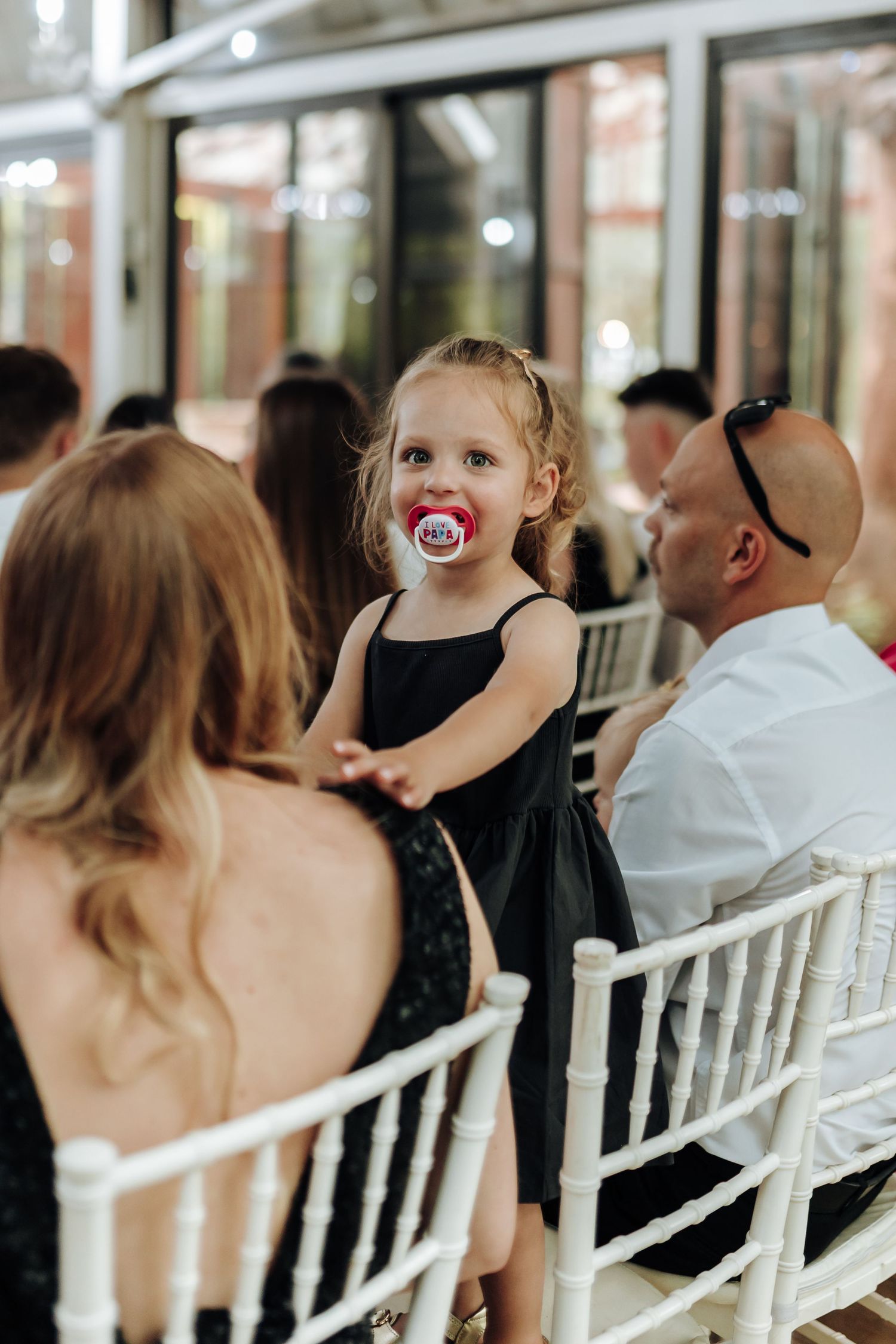 Wedding ceremony guests seated in white chairs at an elegant indoor venue.