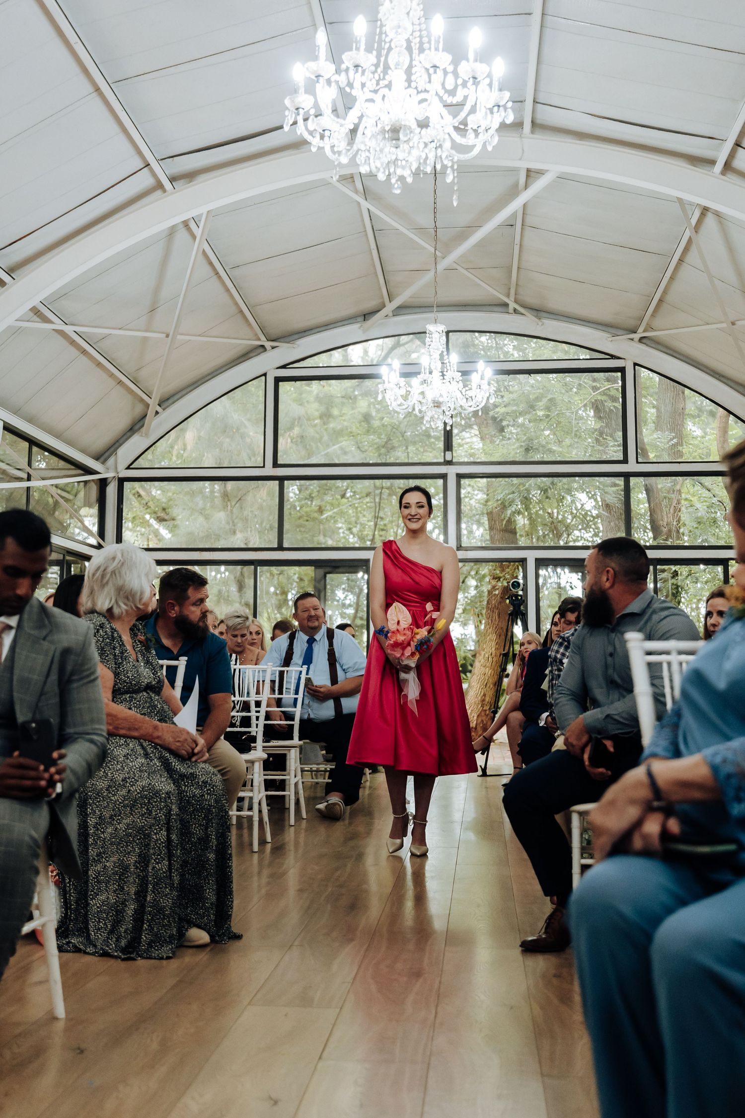 Guests dance together under elegant chandeliers in a bright reception venue with vaulted ceilings.