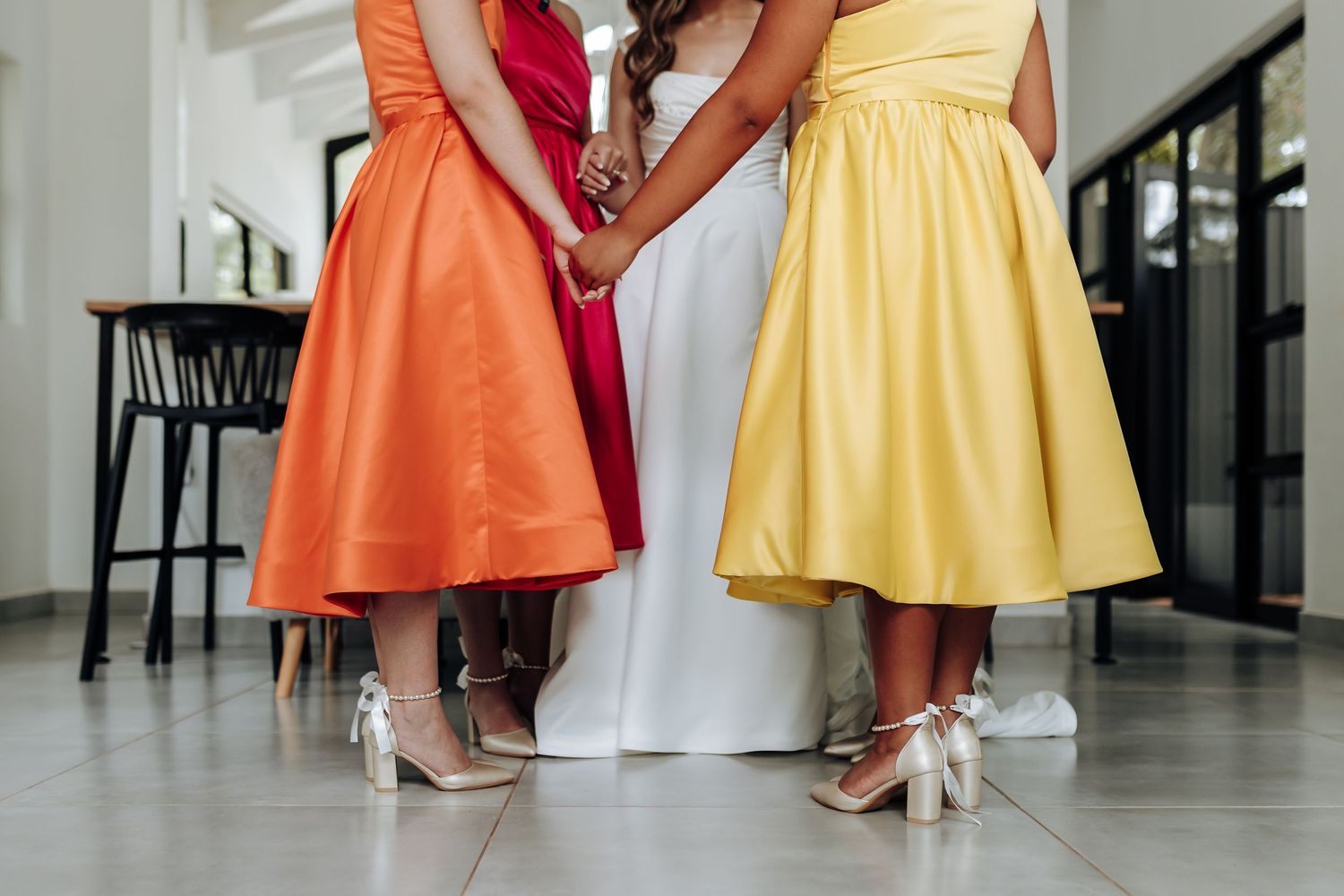Colorful bridesmaid dresses swish and sway as they walk down a bright hallway together.