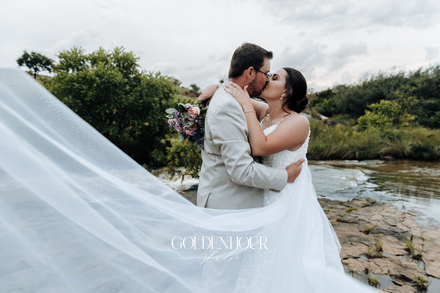 Romantic waterfront wedding portraits with flowing veil against natural scenery.