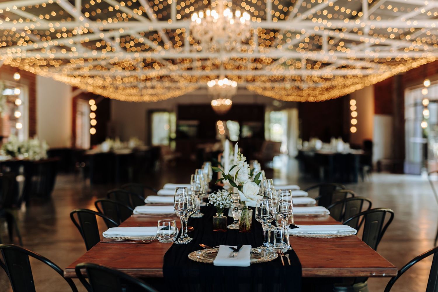 Elegant wedding reception venue with wooden tables and crystal chandeliers creating a warm, romantic atmosphere.