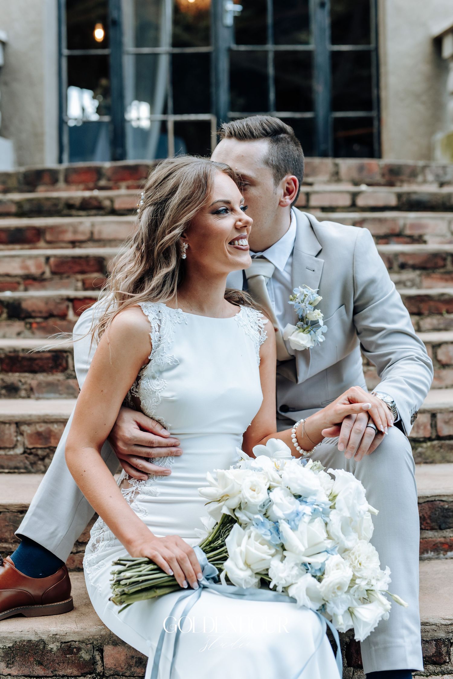 Romantic couple moment with white floral bouquet against brick backdrop.