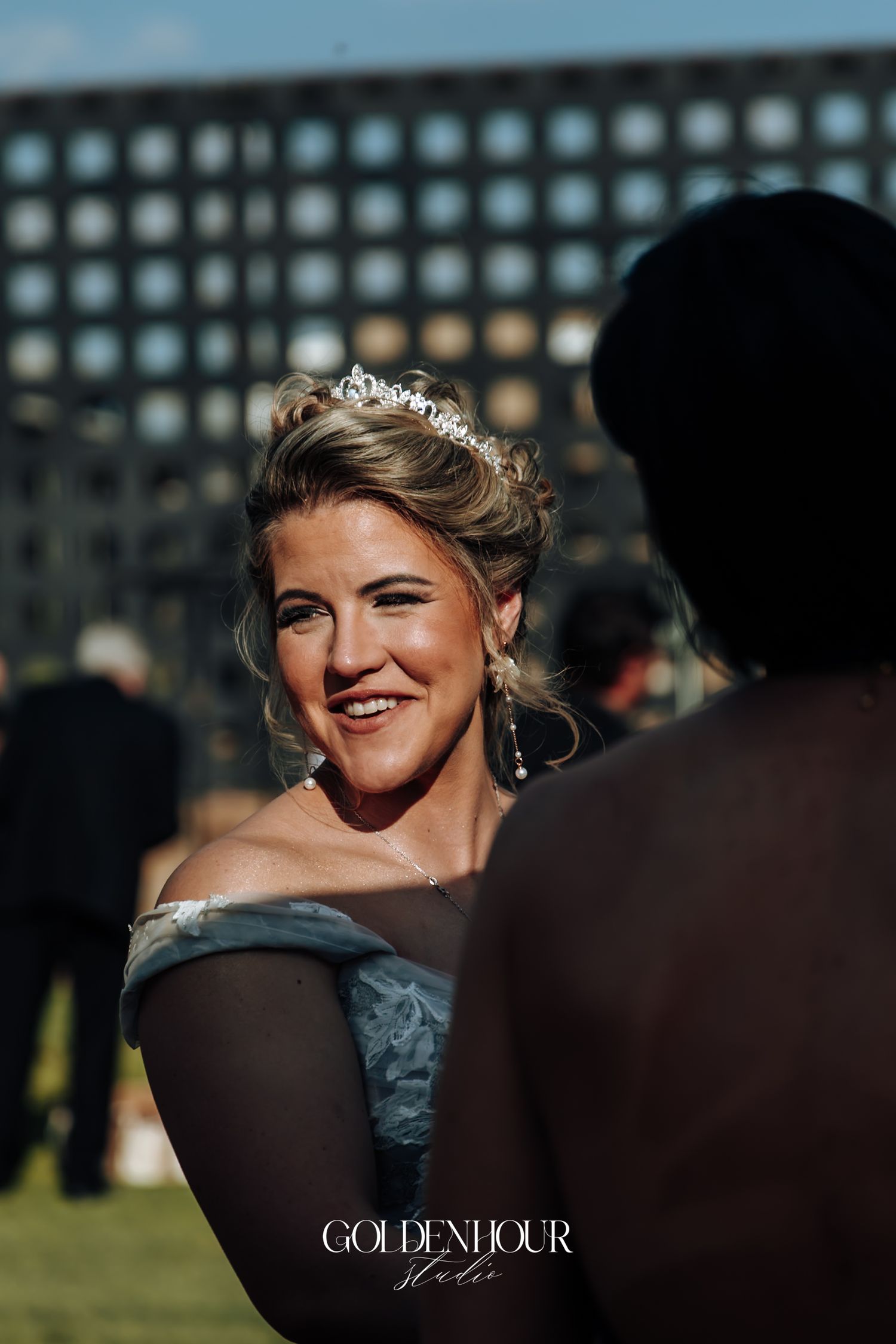 Elegant bride wearing tiara and blue off-shoulder gown smiling at outdoor wedding reception.