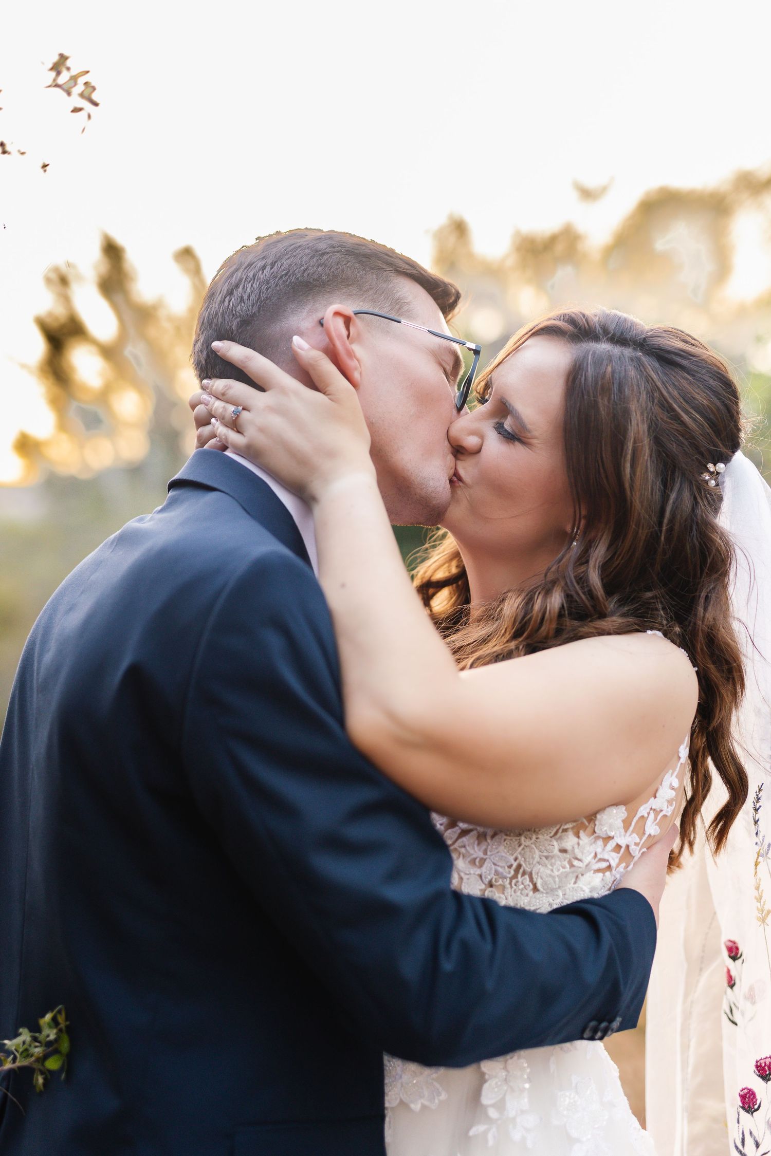 A romantic kiss between newlyweds during sunset at an outdoor wedding ceremony.