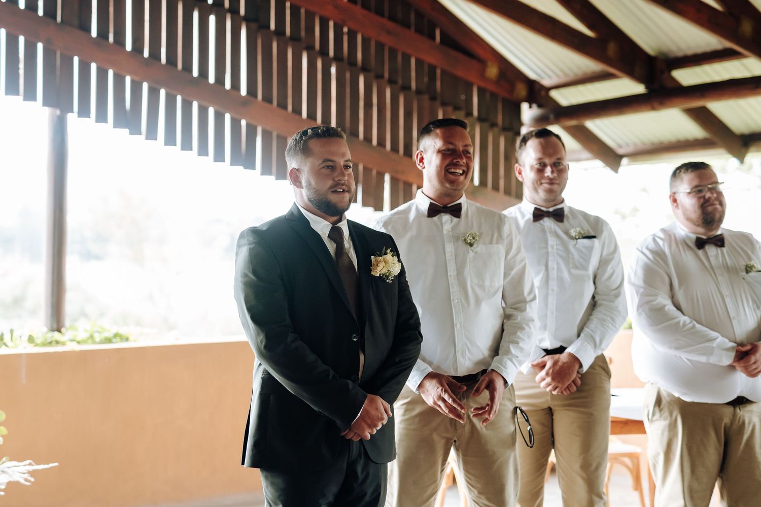 Wedding party members in formal attire stand together under a covered outdoor venue during a celebration.