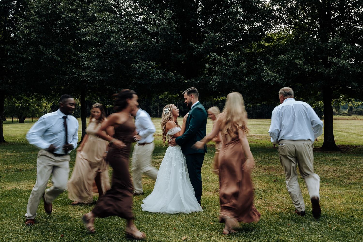 Wedding guests playfully dance and celebrate on a grassy lawn during an outdoor reception.