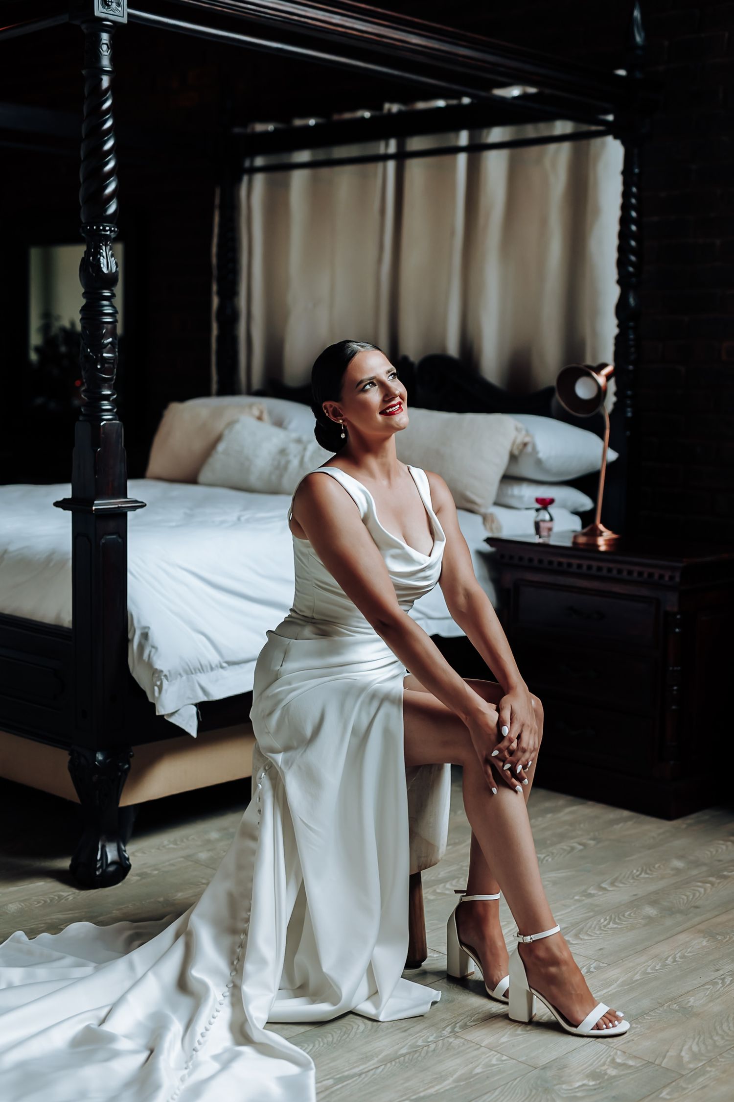 Moody bridal portraits in an elegant bedroom with dark wood furniture and white bedding.