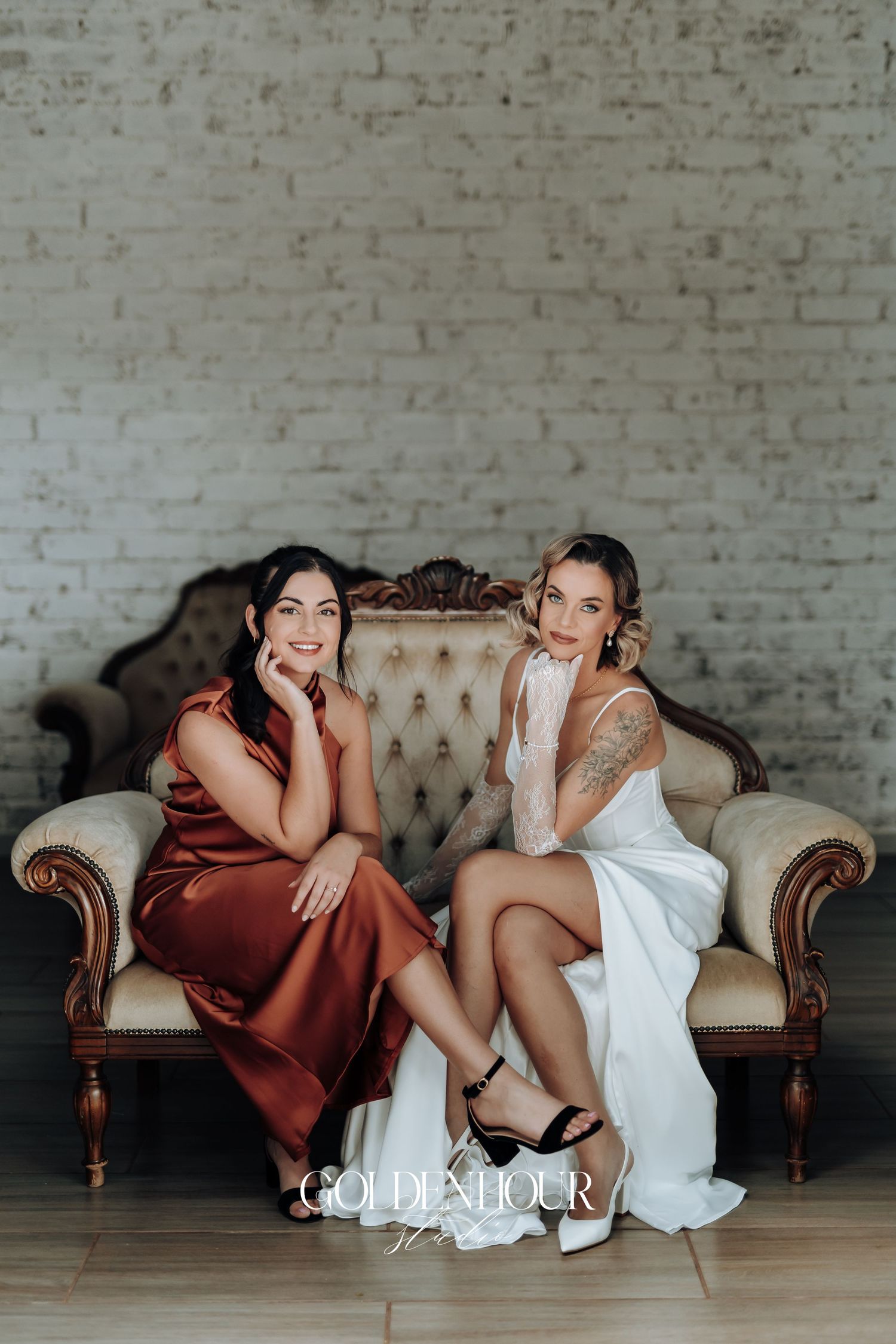 Stylish wedding party lounges on vintage sofa wearing burgundy and white dresses.