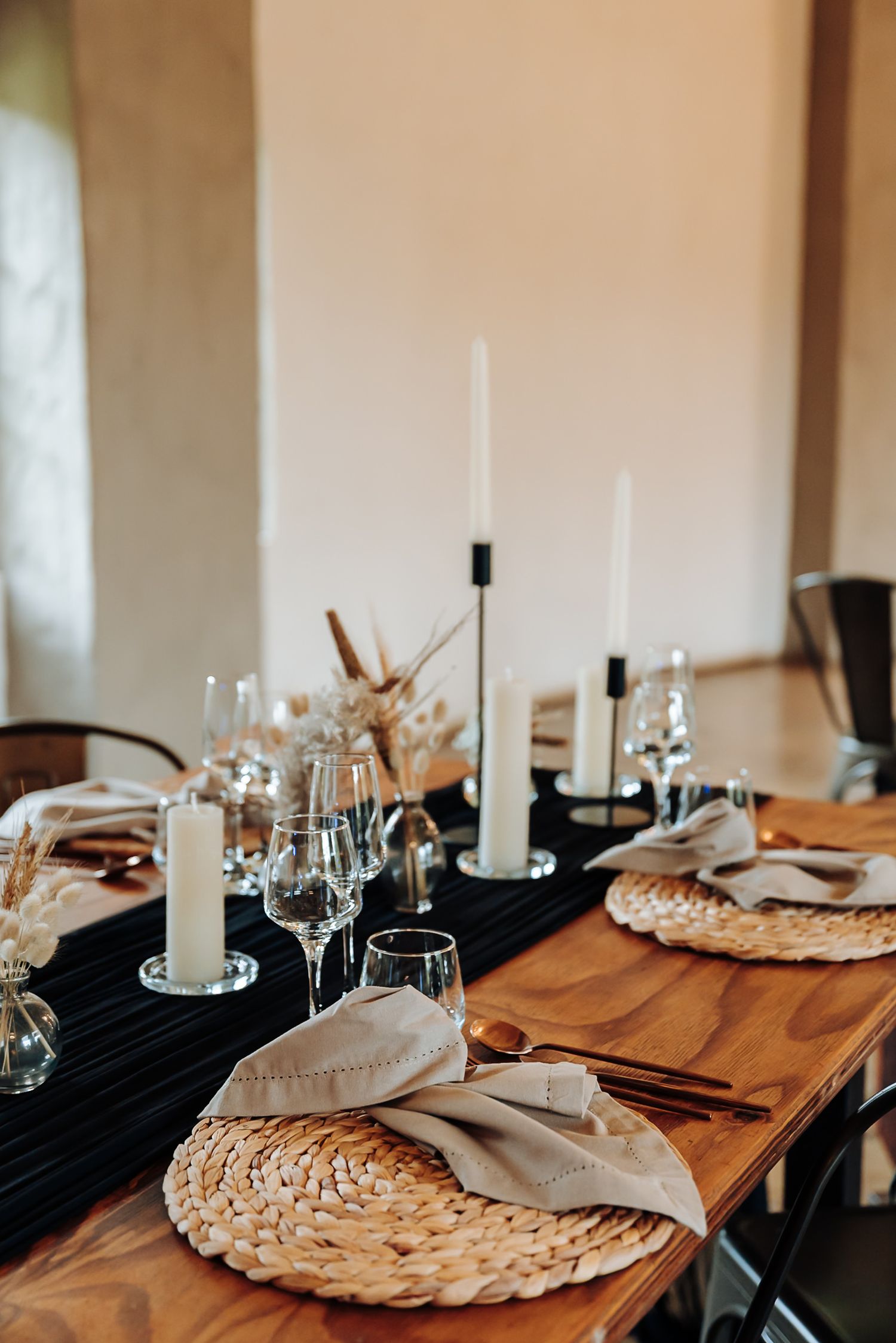 Elegant table setting with woven placemats, white candles, and wine glasses on a wooden dining table.