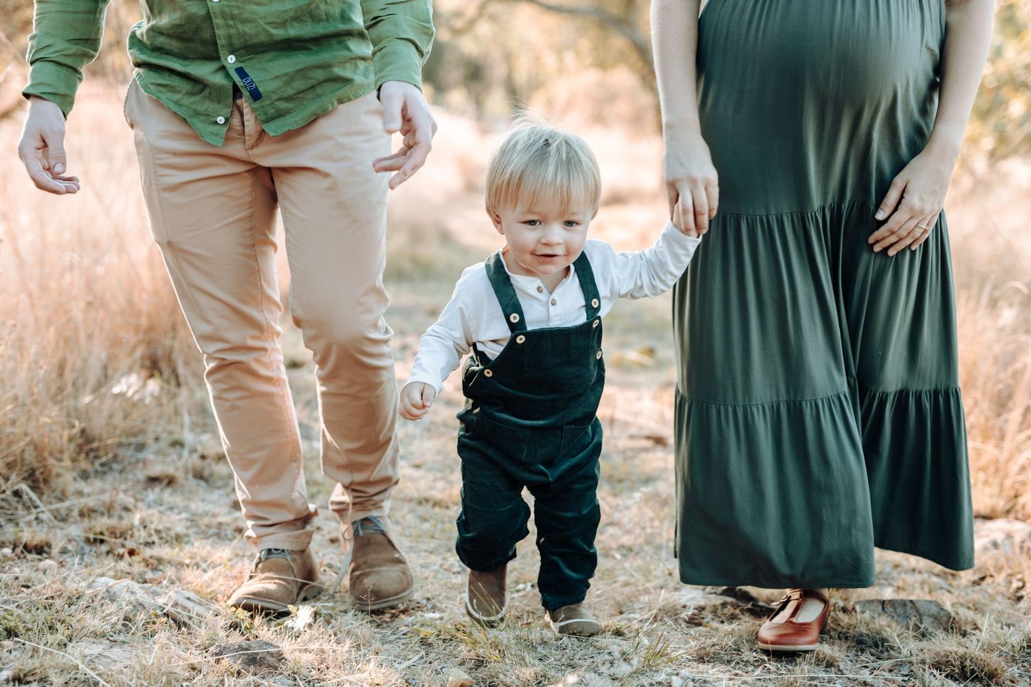 Family wearing coordinating green and khaki outfits walking together in an outdoor natural setting at sunset.