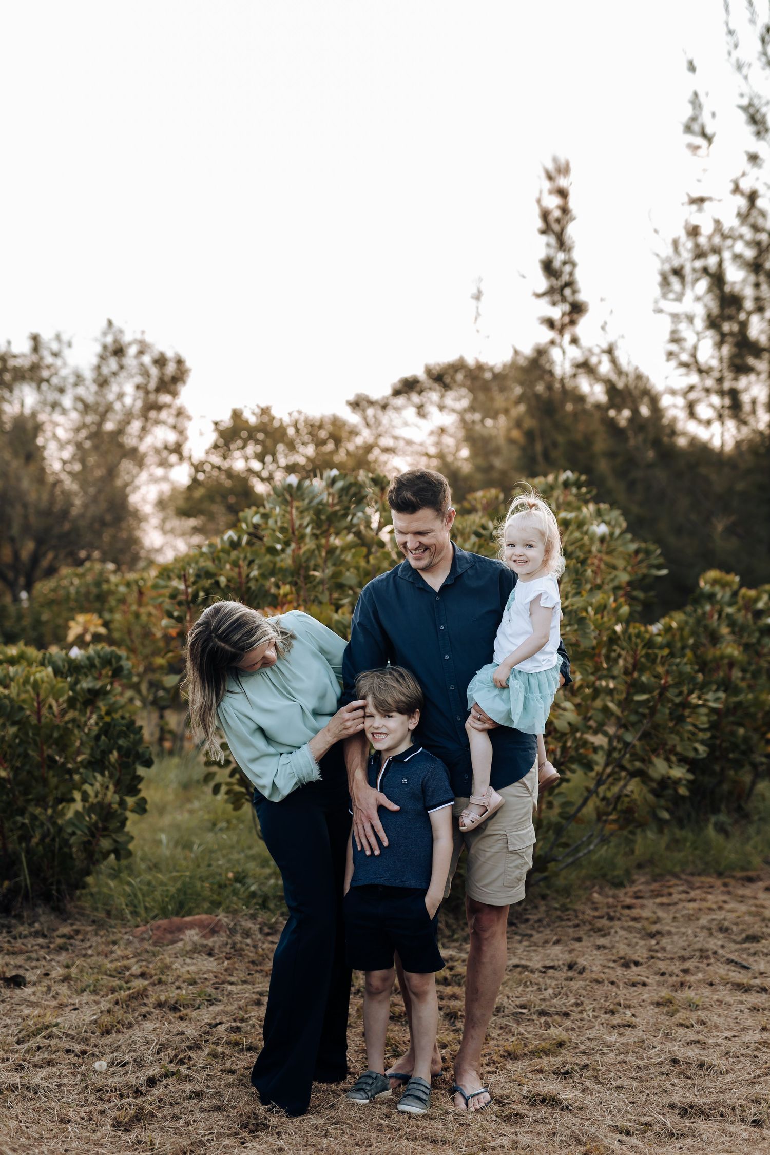 A joyful family moment captured during golden hour in an outdoor setting with natural foliage.