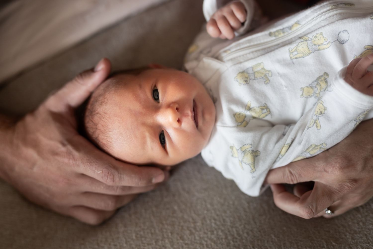 A series of images showing gentle hands holding and comforting a newborn baby in a white patterned onesie.