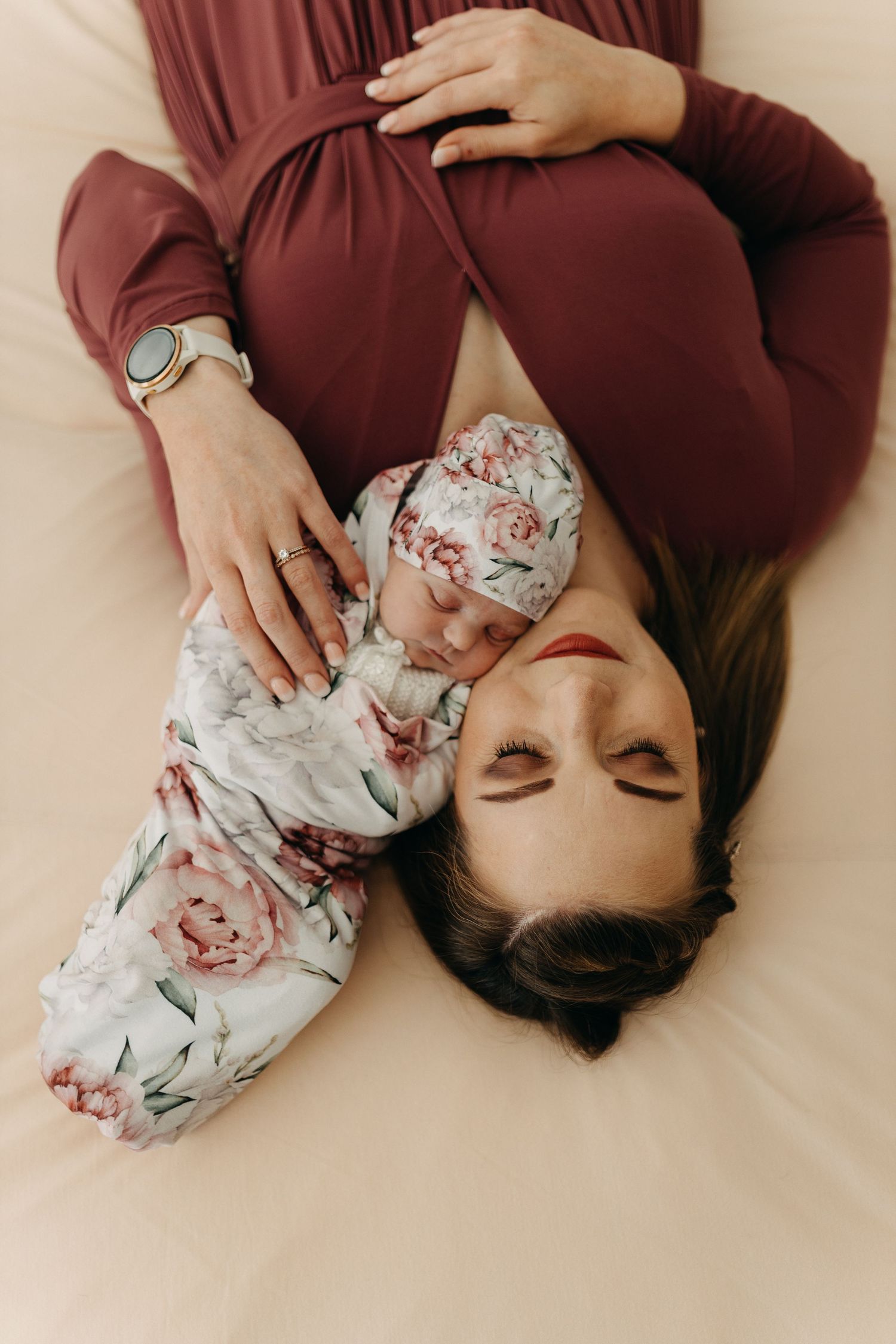 Top view of baby and parent resting together on white bedding wearing burgundy and floral prints.