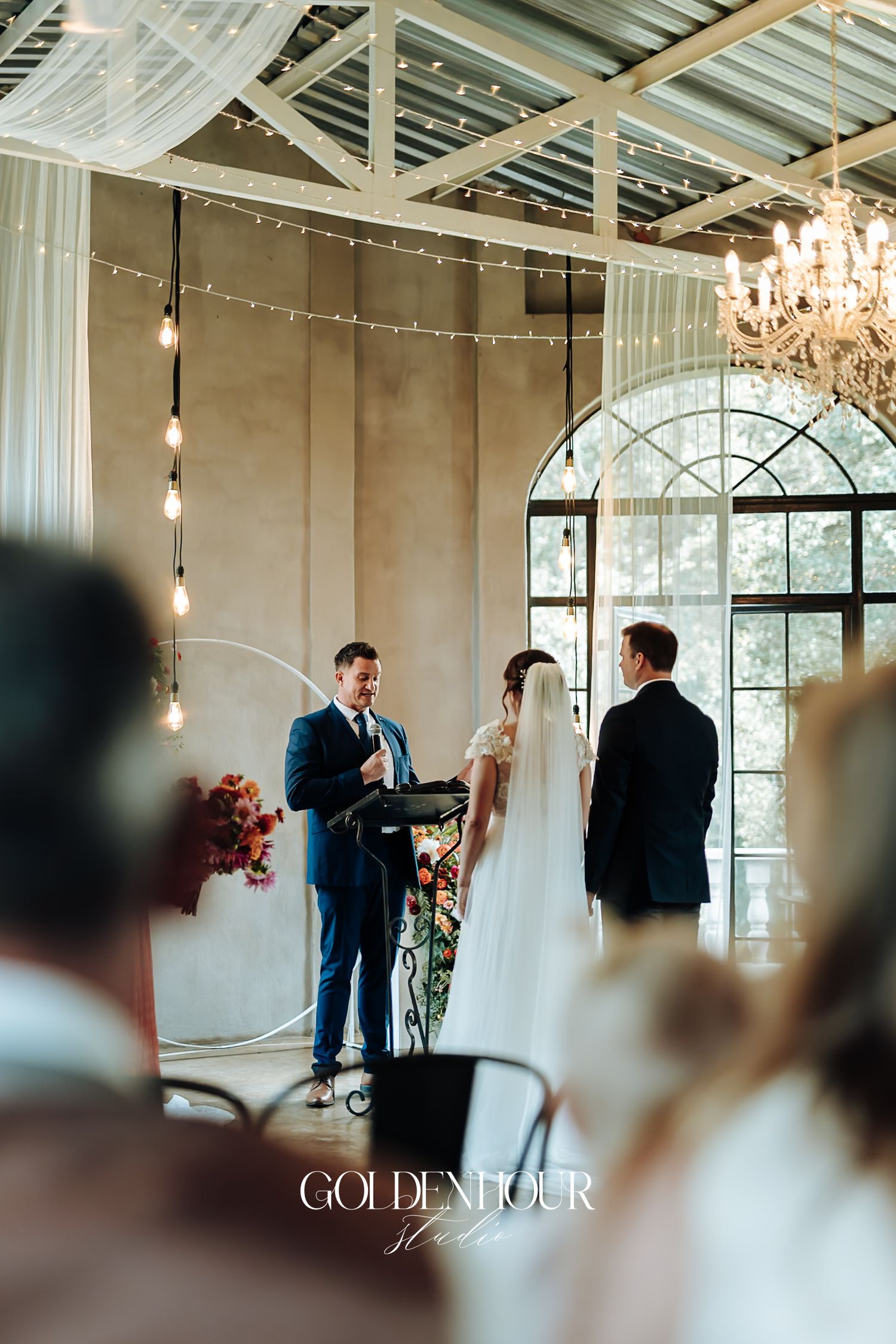 Officiant reading vows as bride and groom stand at altar in bright chandelier-lit ceremony hall.