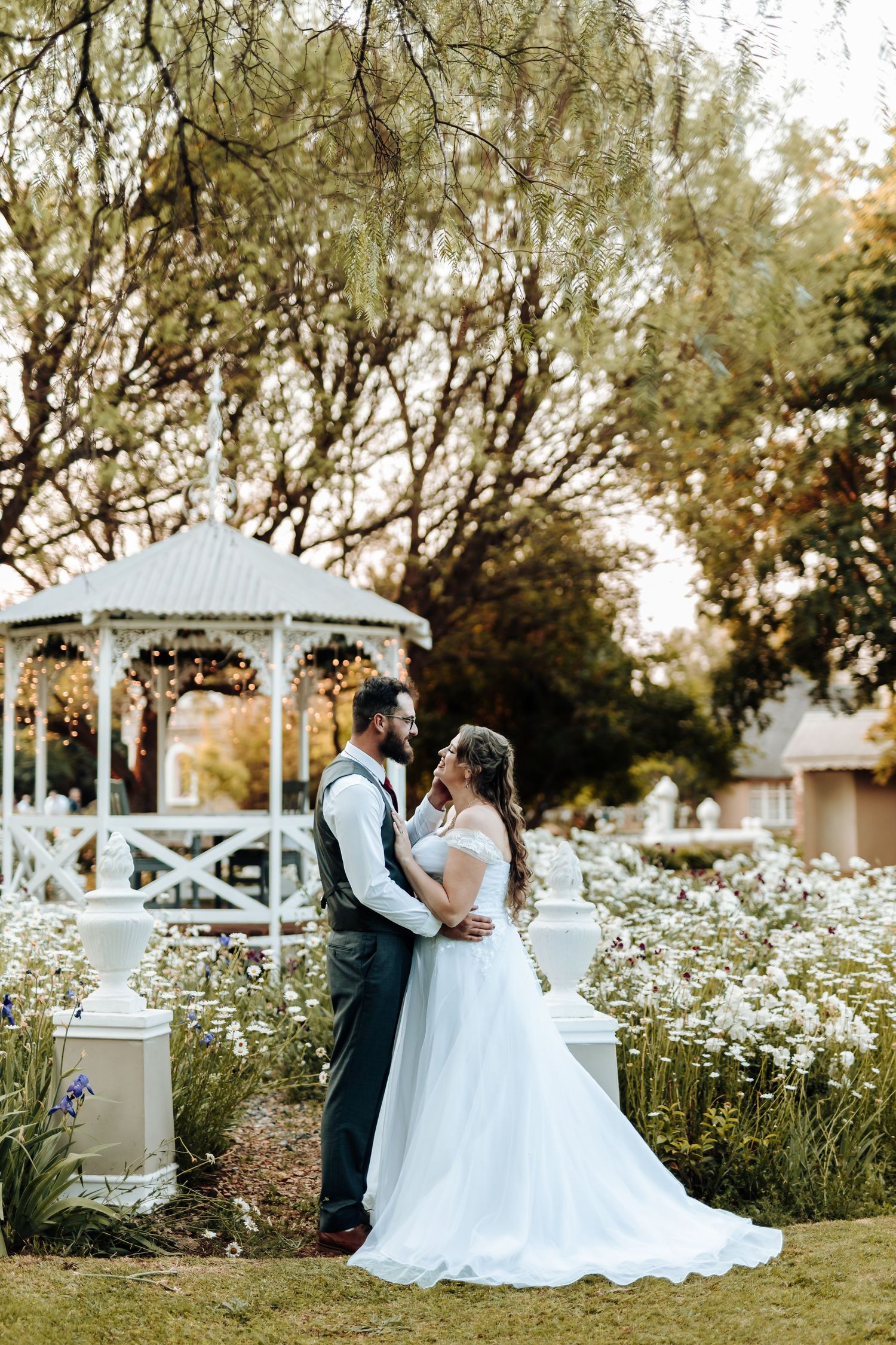 Intimate wedding portrait of couple against white garden gazebo and blooming wildflowers.