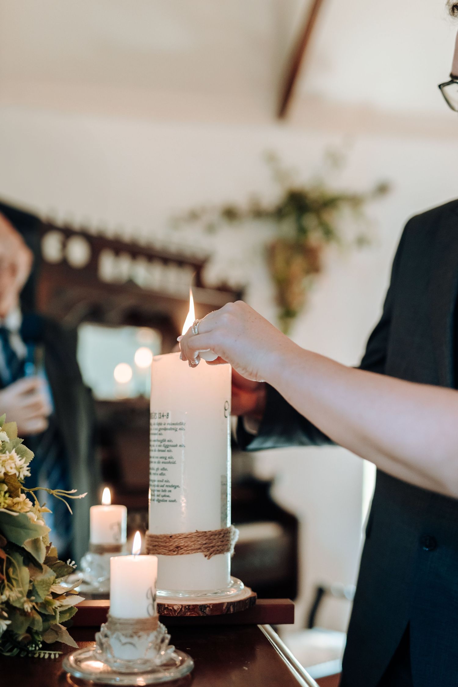 Close-up of hands lighting a unity candle wrapped in twine during wedding ceremony.