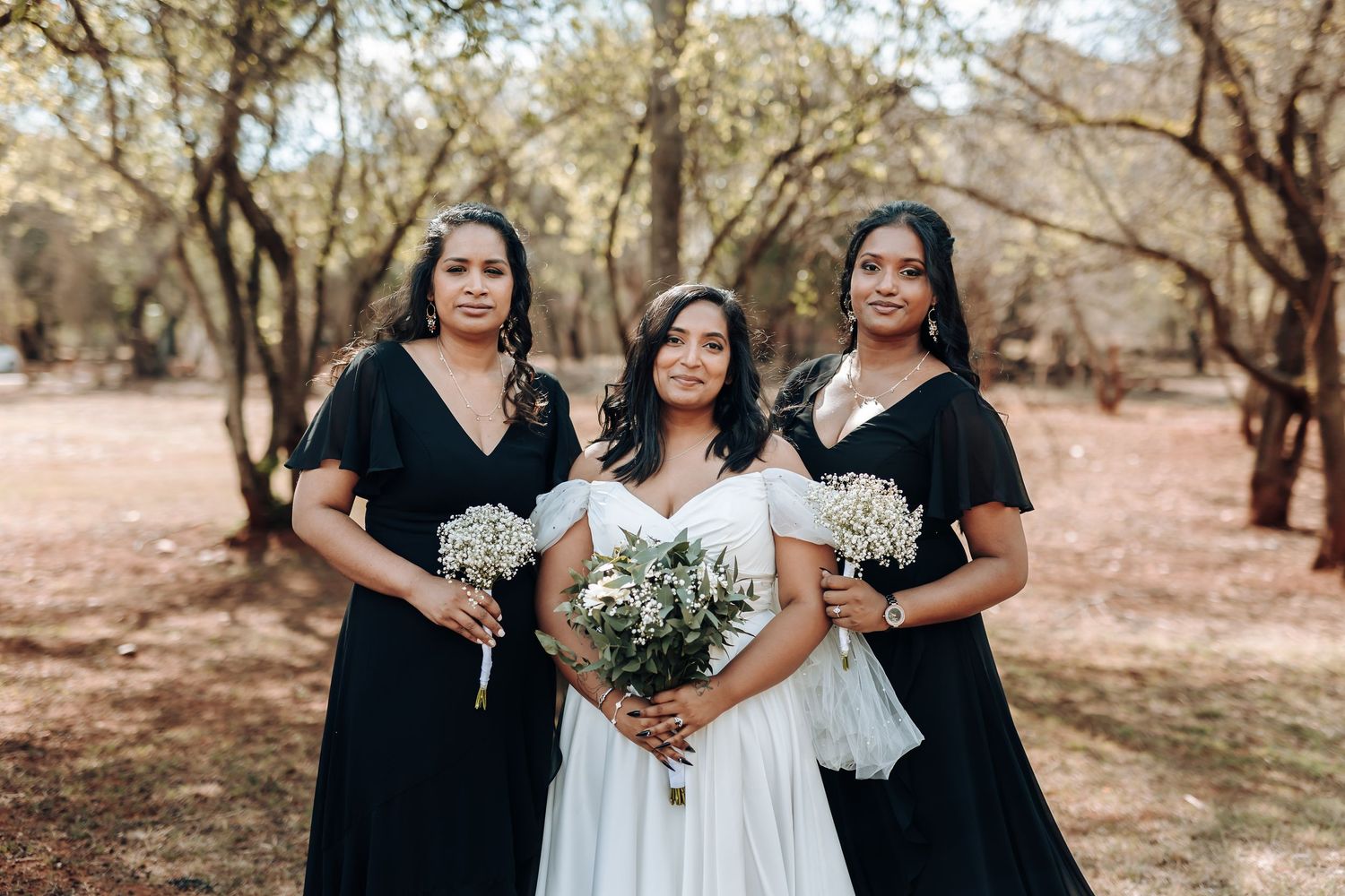 Bride in white gown with bridesmaids in black dresses holding bouquets.