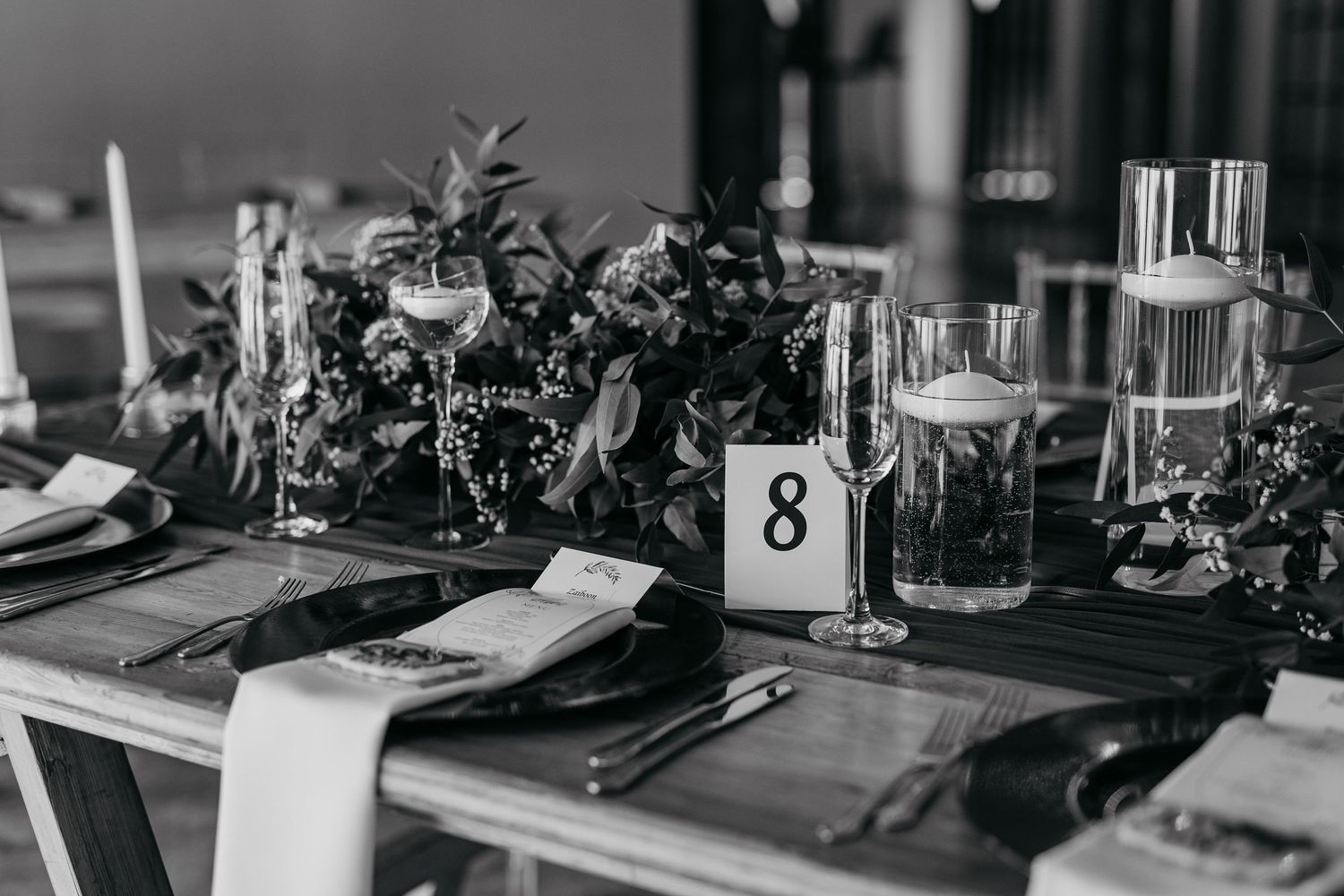 Black and white photo of elegant table setting with floral centerpiece and table number eight.