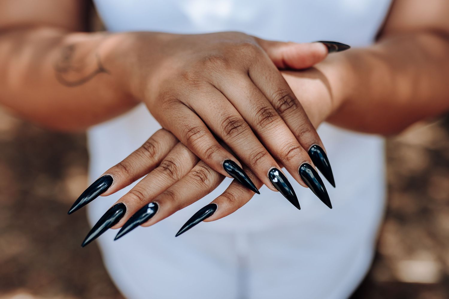 Close-up of hands with long black stiletto nails against white fabric background.