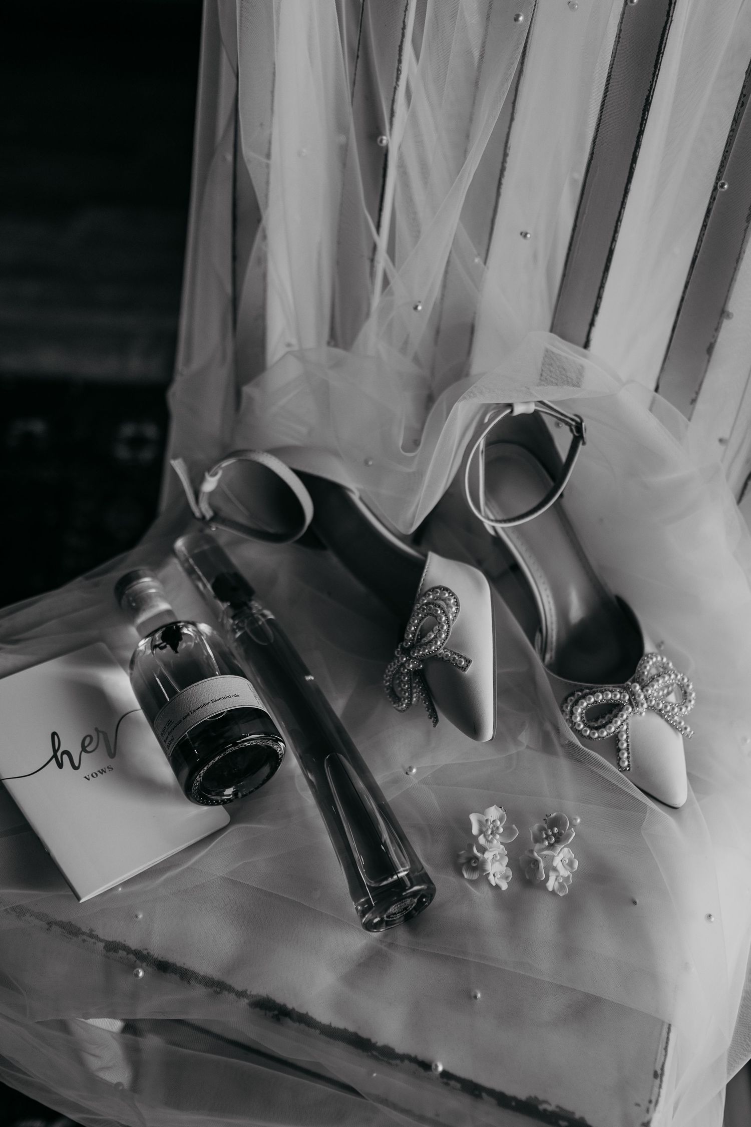 Elegant bridal shoes with crystal bow details next to a champagne bottle and accessories in black and white.