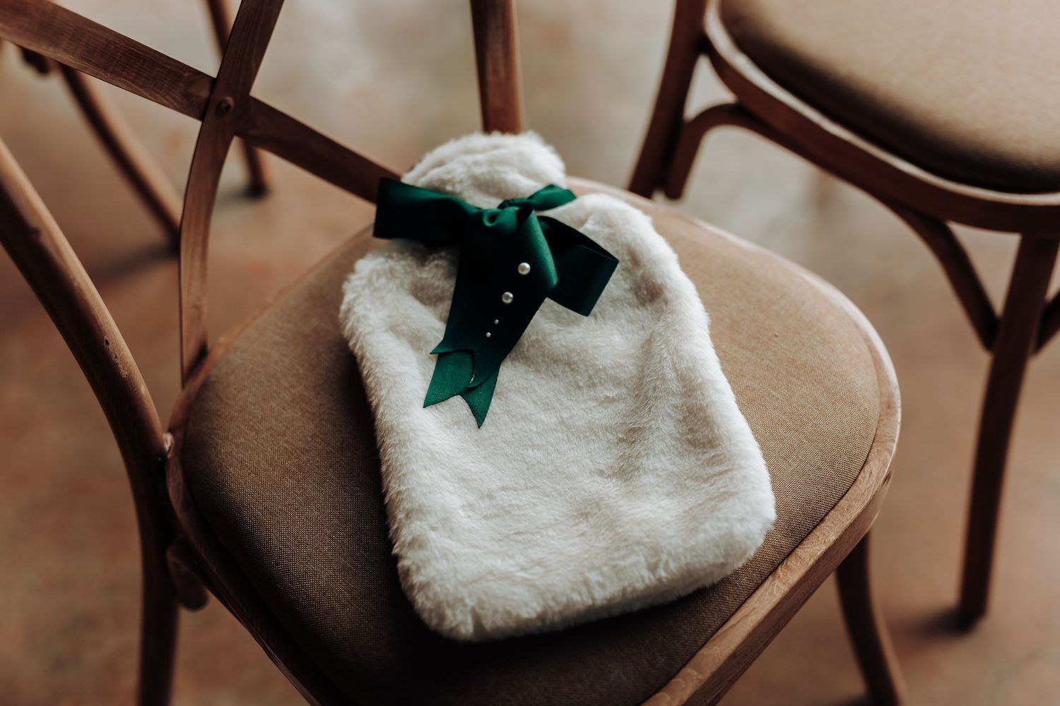 White furry bag with green bow sitting on a wooden chair.