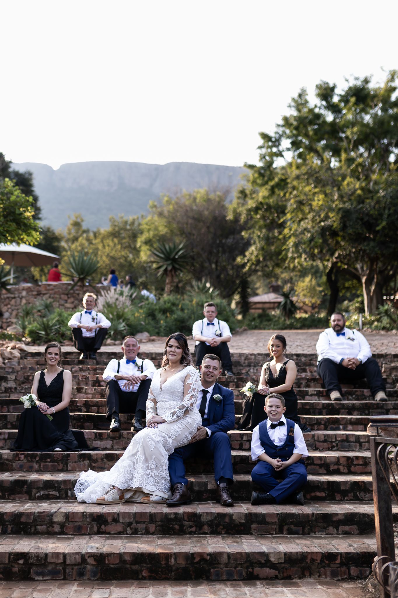 Wedding party poses on stone steps with scenic mountain backdrop.