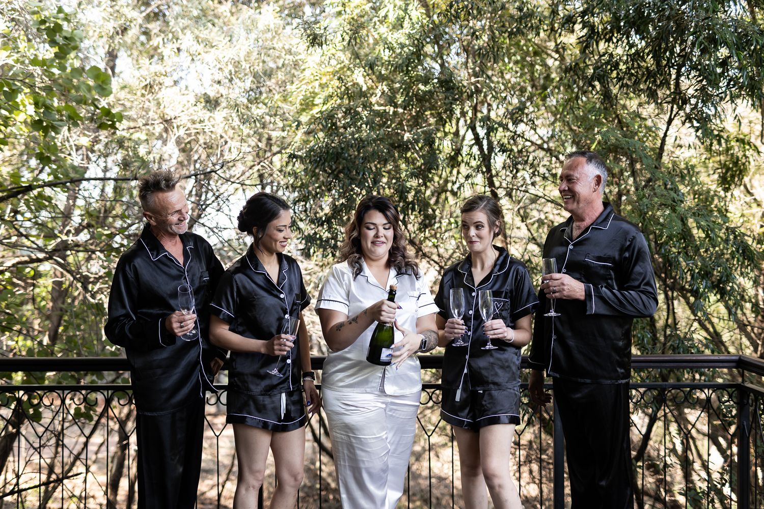 Wedding party in matching black outfits posing together outdoors.