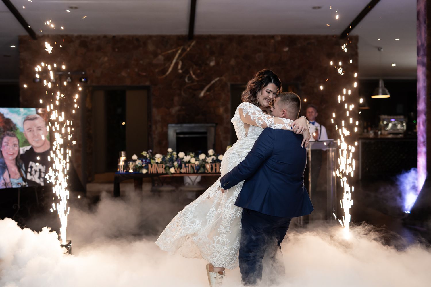 Romantic dance moment captured with fog effects and sparkler fountains at wedding reception.