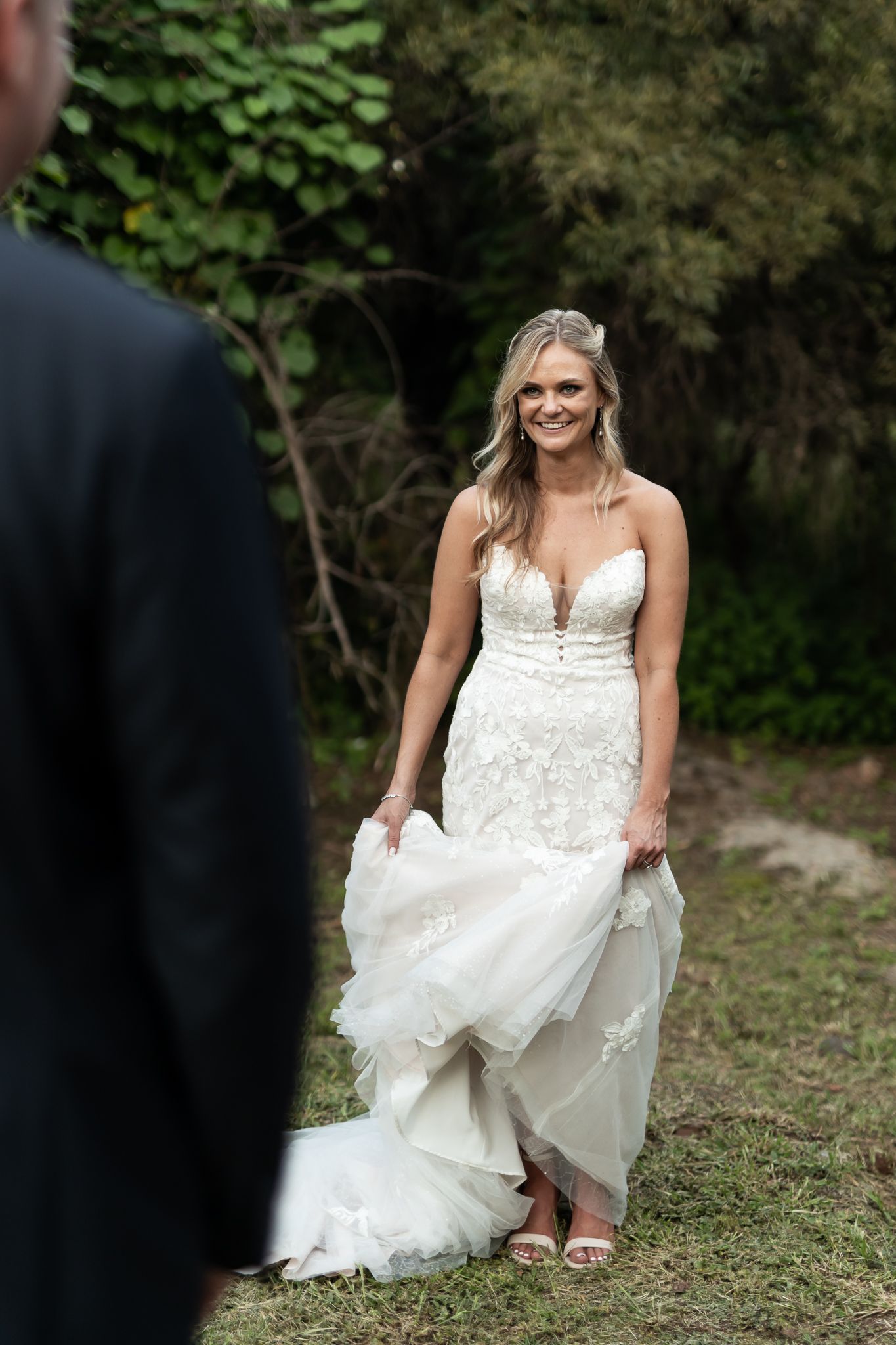 Bride in a fitted lace gown poses in a natural outdoor setting.