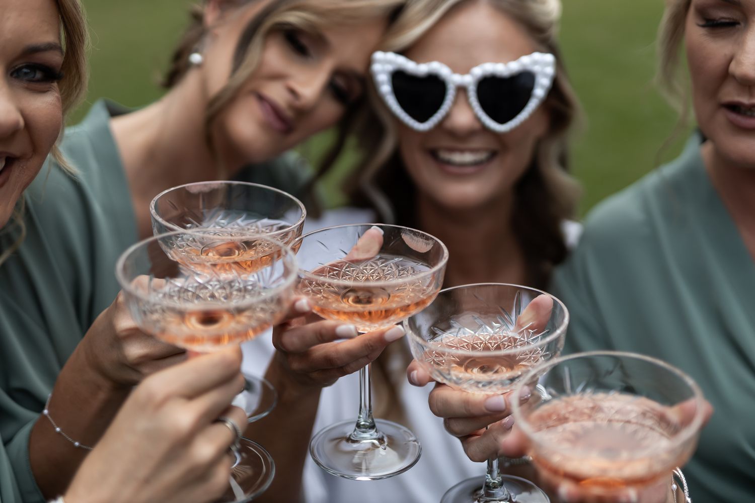 Close-up of champagne glasses being toasted by bridesmaids in matching outfits.
