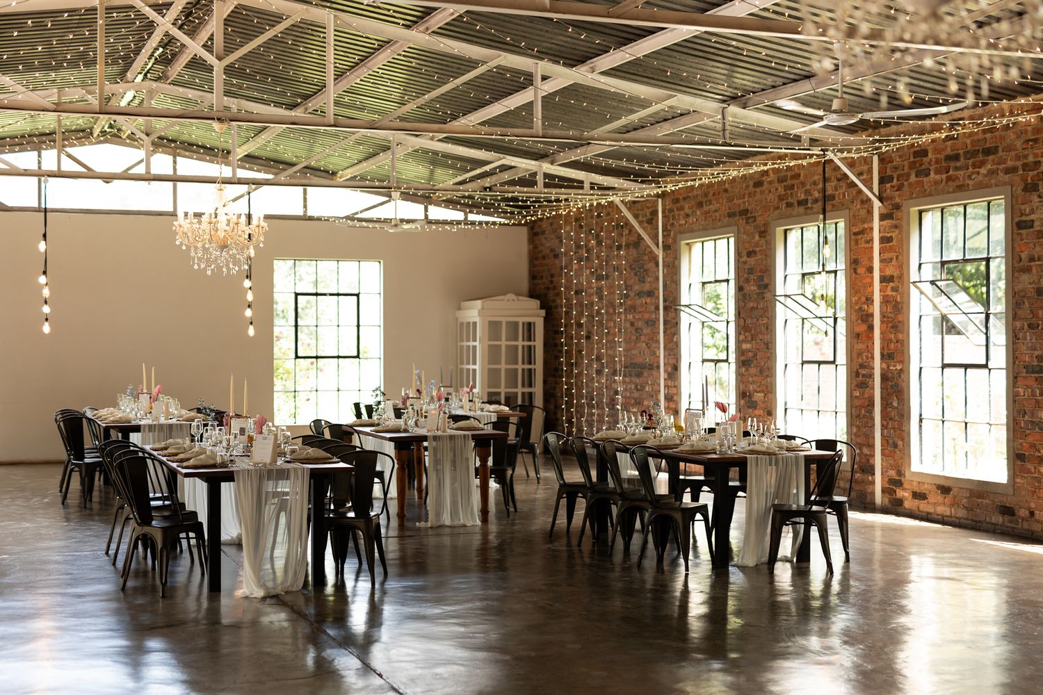 Light-filled industrial wedding venue with exposed brick walls and modern minimal table settings.